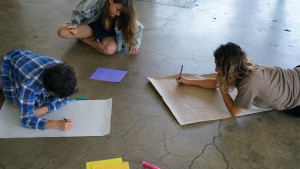 3 people writing on craft paper, on the floor